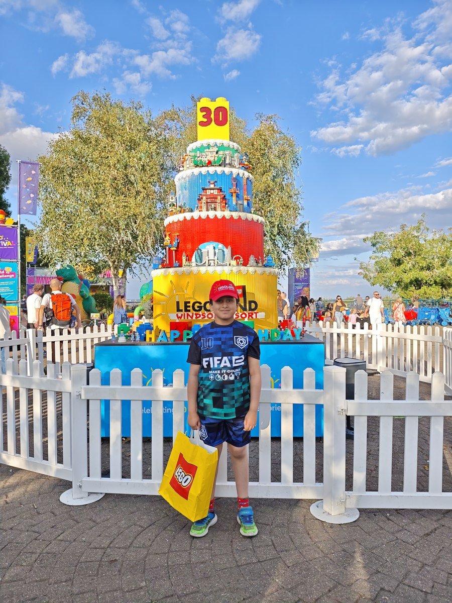 Bhuvan smiling, holding a LEGO bag in front of a giant LEGO birthday cake
